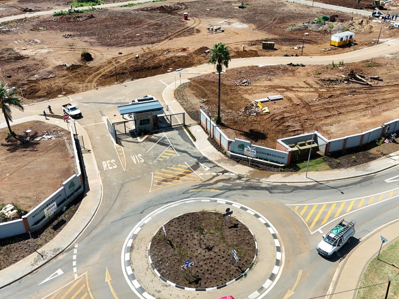 Aerial view of a residential estate entrance featuring a security gatehouse, perimeter walling, and a paved roundabout access point.