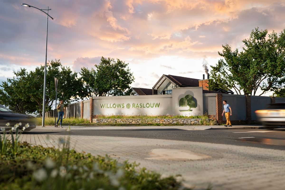 Street view of the Willows at Raslouw estate entrance, featuring a well-maintained boundary wall, signage, and paved sidewalk infrastructure.