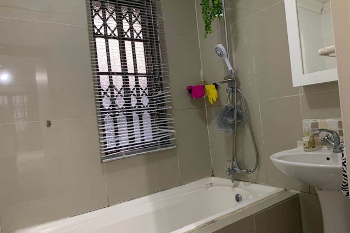 A functional bathroom featuring a bathtub with a handheld shower attachment, a pedestal basin, and tiled walls.