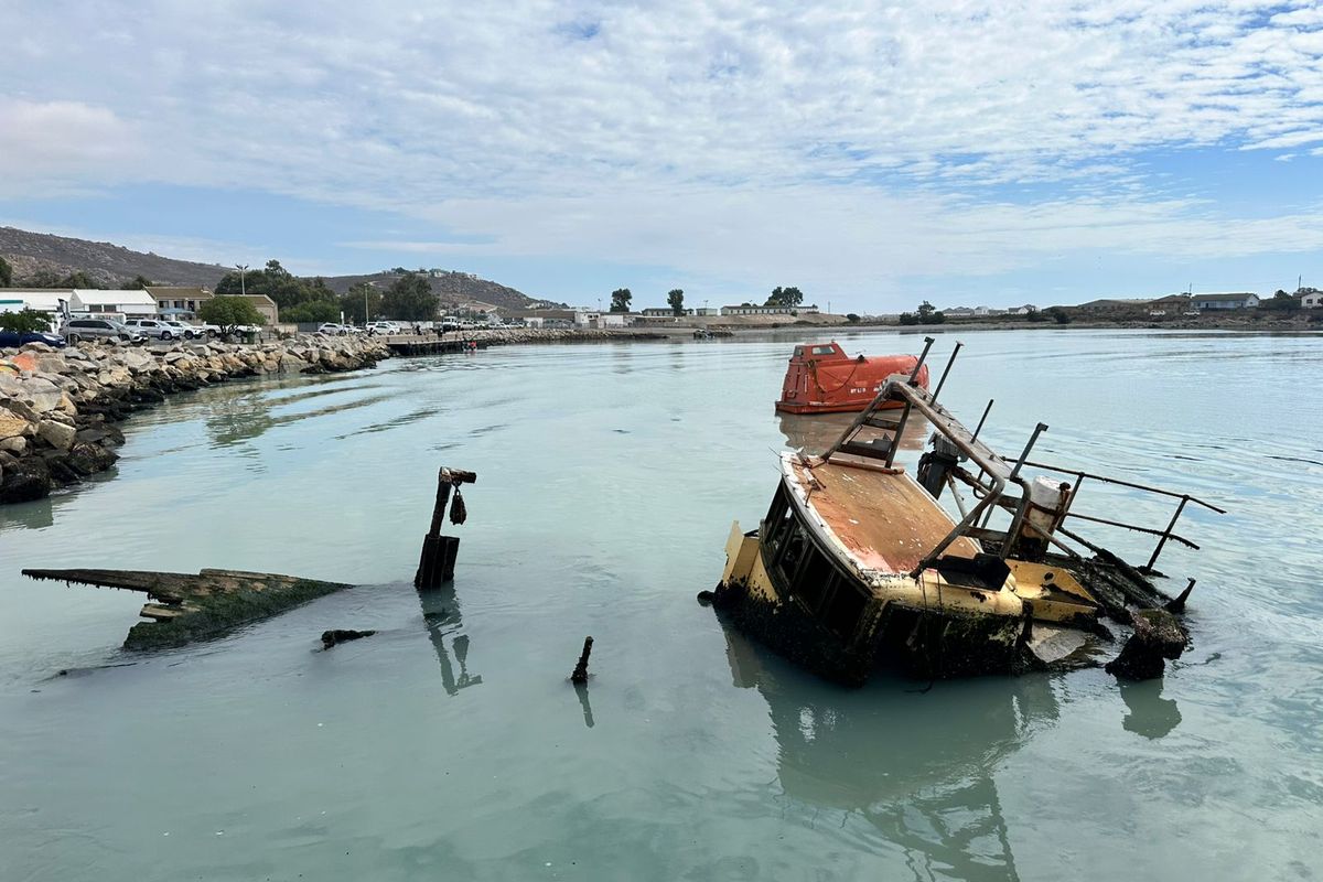 A view of a coastal area featuring partially submerged boat wreckage in the water.