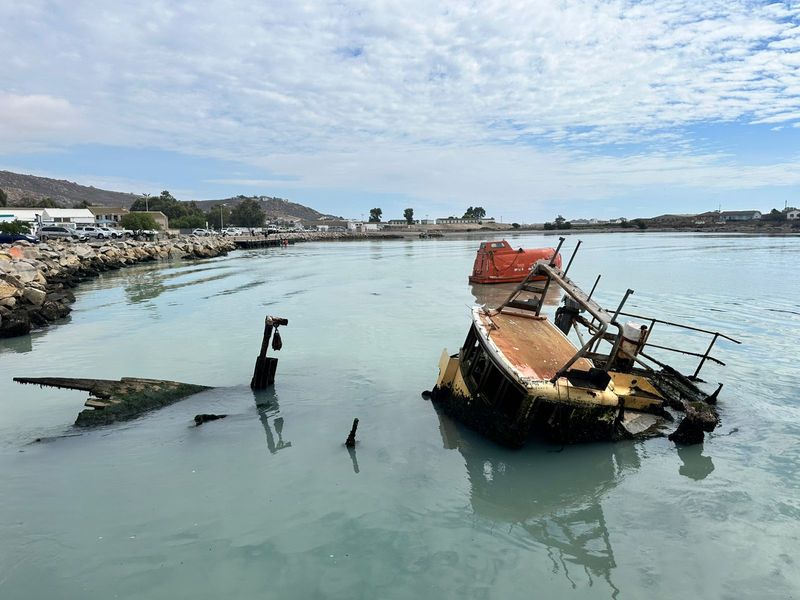 A view of a coastal area featuring partially submerged boat wreckage in the water.