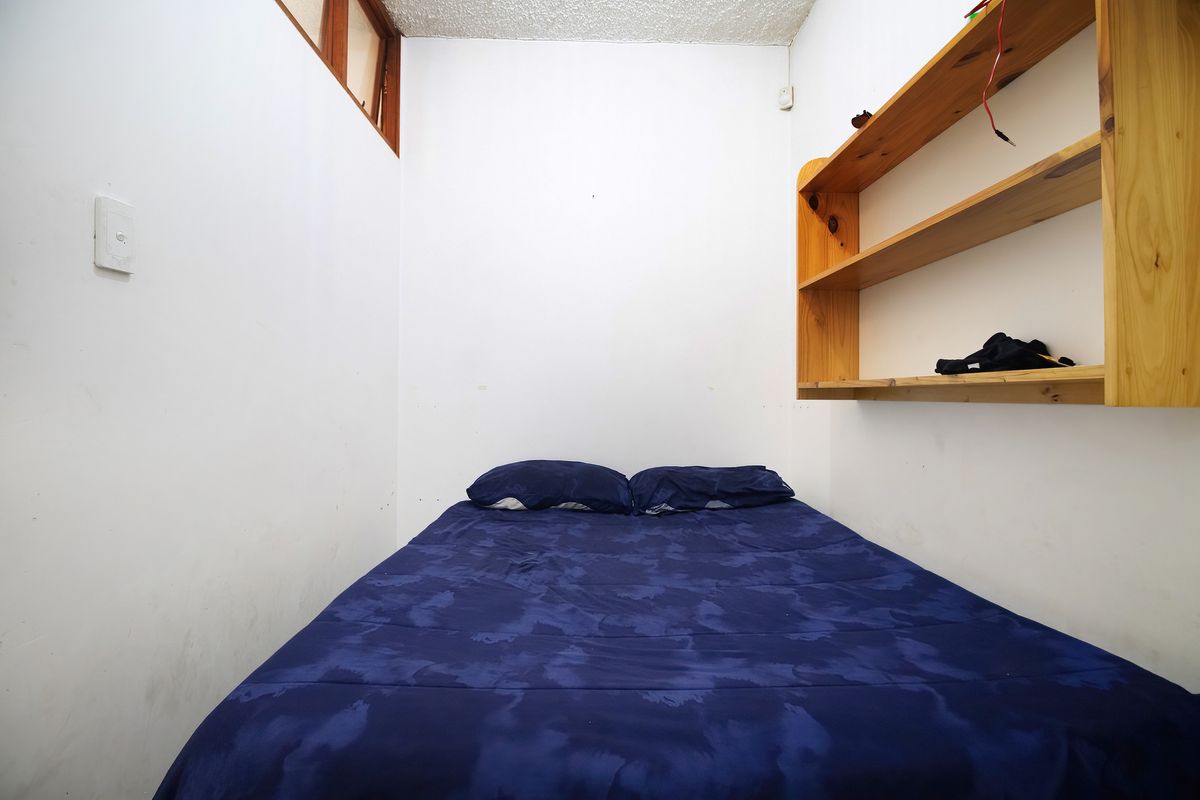 A compact bedroom featuring built-in wooden shelving and a high-level window, providing natural light to the space.