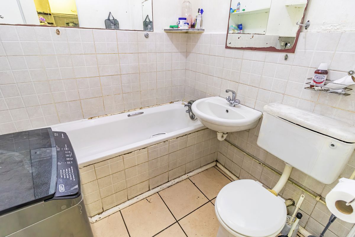 A dated bathroom featuring a bathtub, wall-mounted basin, and toilet with tiled finishes, requiring renovation to modernize the space.