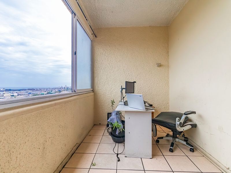 Enclosed balcony space featuring tiled flooring and large sliding windows with expansive city and coastal views.