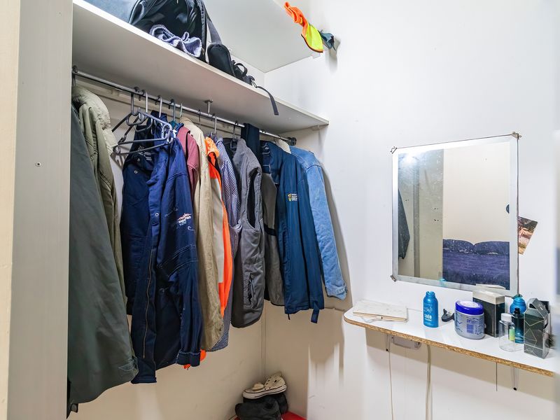 A functional bedroom closet area featuring built-in shelving, a hanging rail, and a wall-mounted mirror with a small vanity shelf.
