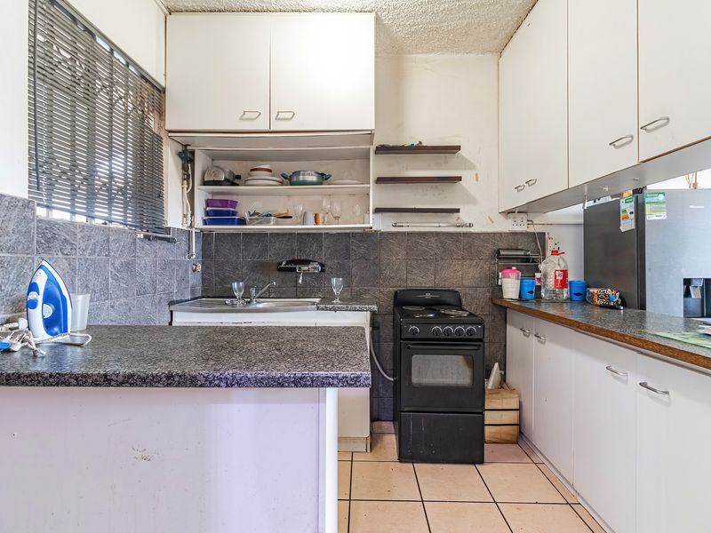A functional kitchen featuring white built-in cabinetry, granite countertops, a tiled backsplash, and a freestanding stove, offering potential for modernization.