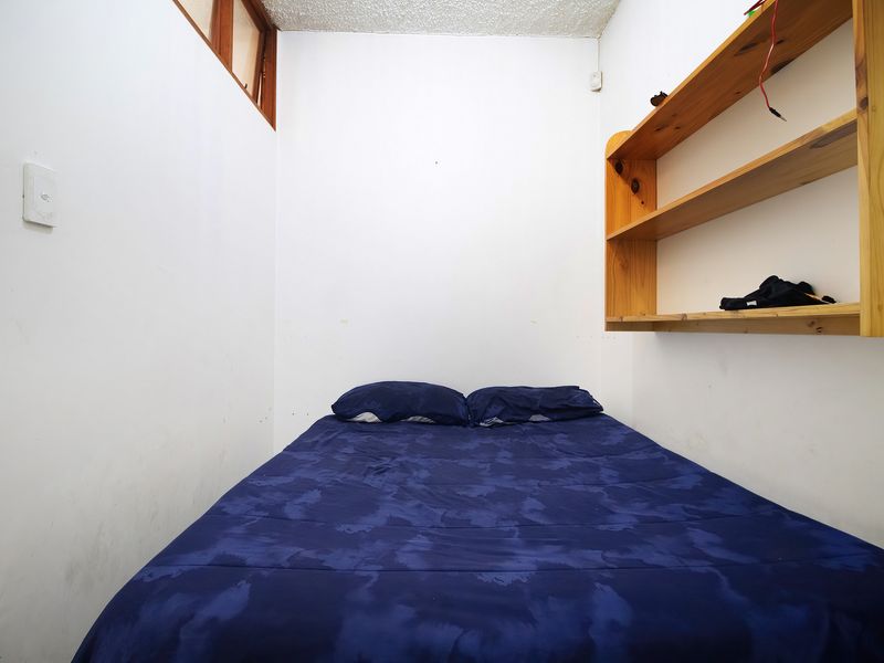 A compact bedroom featuring built-in wooden shelving and a high-level window, providing natural light to the space.
