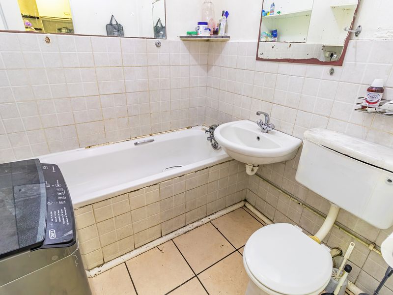 A dated bathroom featuring a bathtub, wall-mounted basin, and toilet with tiled finishes, requiring renovation to modernize the space.