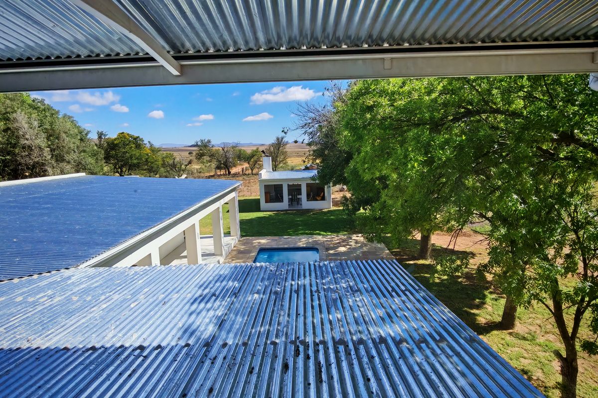 Elevated view overlooking the farm property, featuring a swimming pool, landscaped garden, and a detached outbuilding under a clear blue sky.
