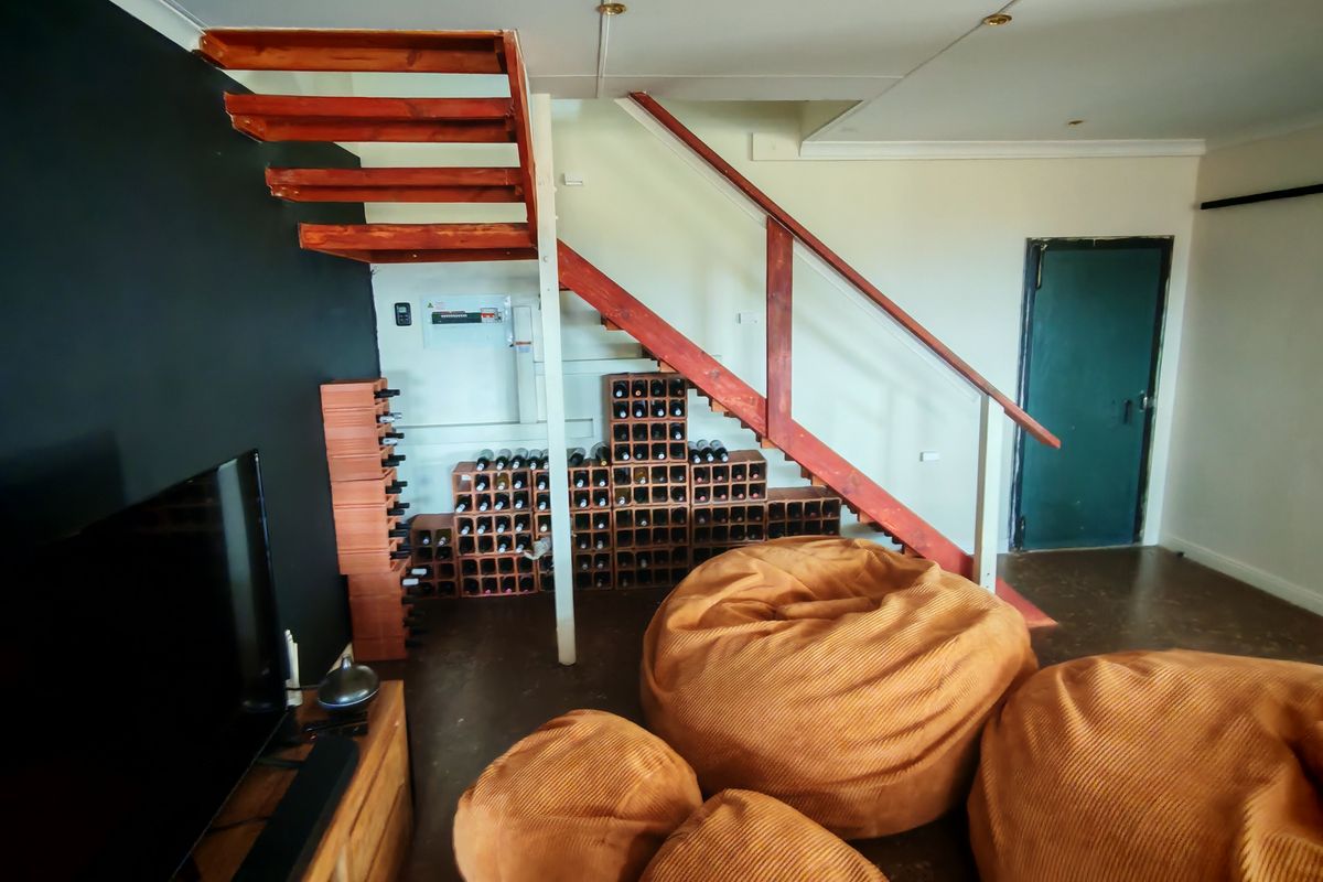Living area featuring an open-tread wooden staircase with integrated brick wine storage underneath and a solid timber door.