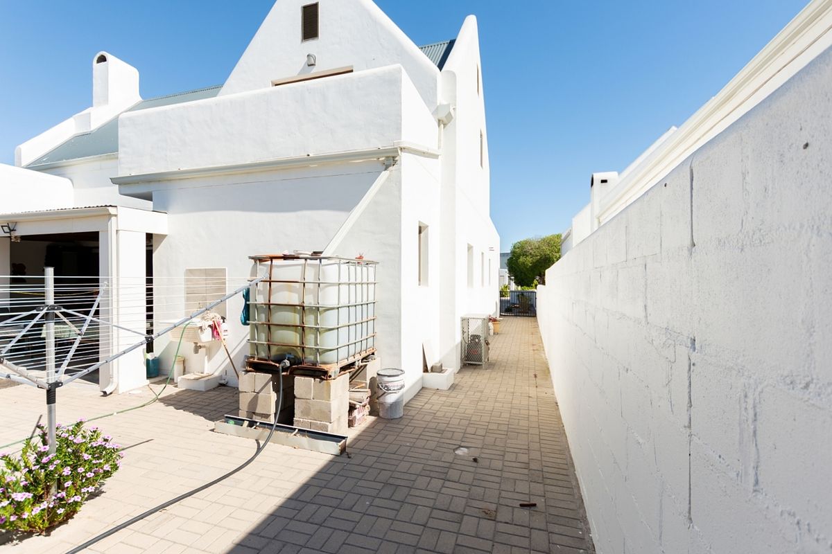 A side exterior view of the property featuring a paved walkway, boundary wall, and a water tank installation.