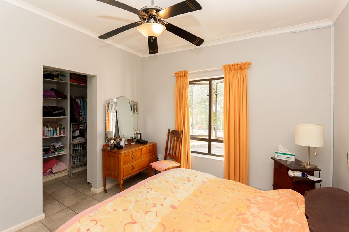 A functional bedroom featuring a ceiling fan, tiled flooring, and a built-in closet with open shelving.