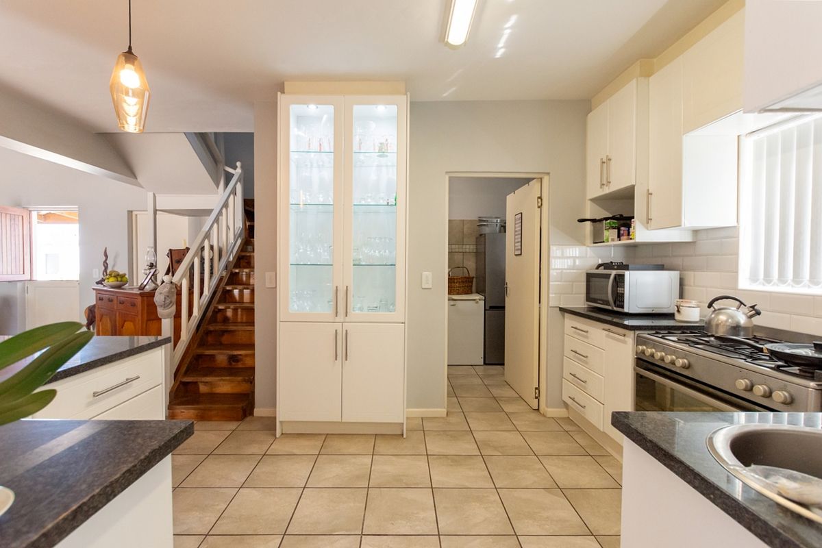A well-maintained kitchen featuring white cabinetry, stone countertops, a gas stove, and a built-in glass display cabinet, with an adjacent staircase.