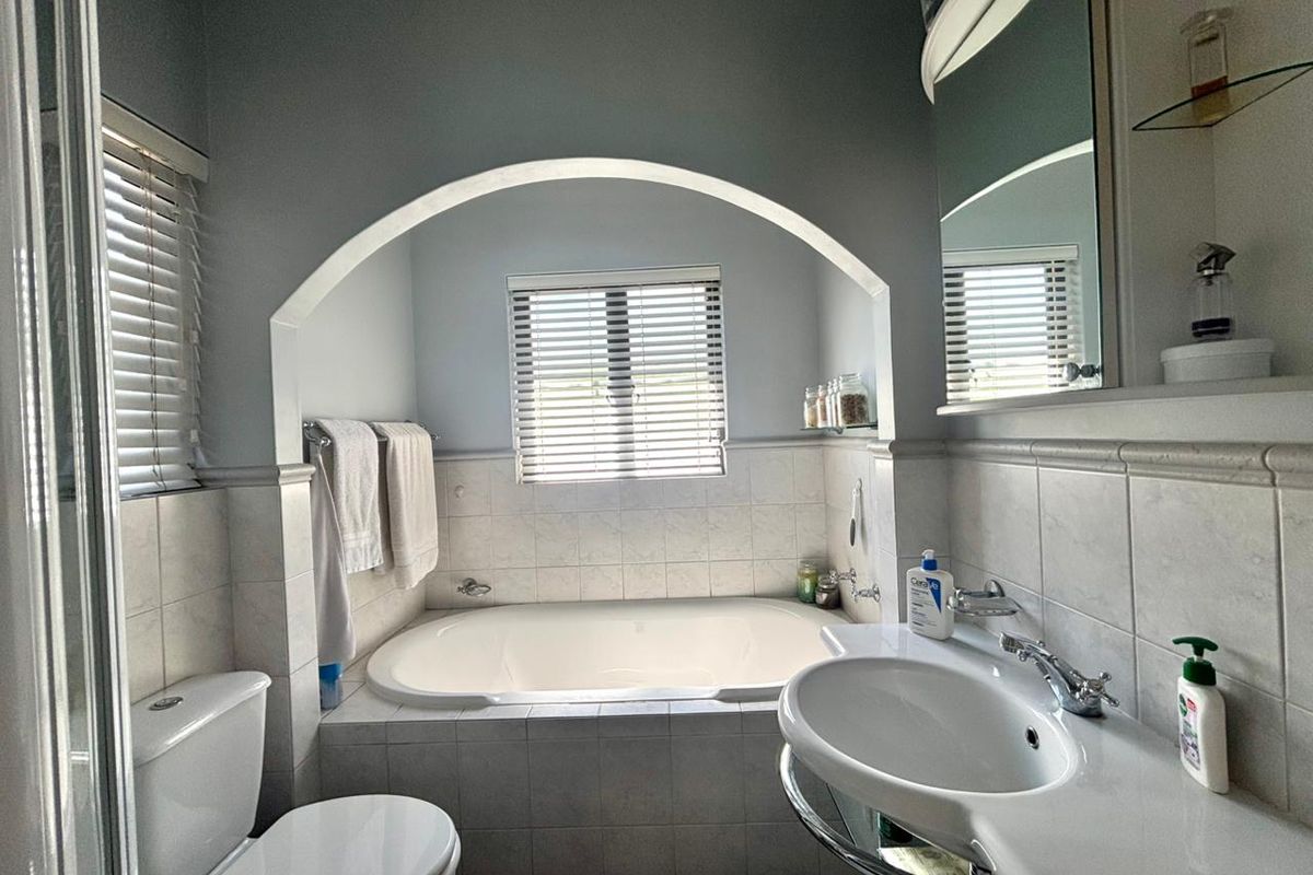 A functional bathroom featuring a built-in bathtub set within an arched alcove, tiled wall surrounds, and a pedestal washbasin with a mirrored medicine cabinet.