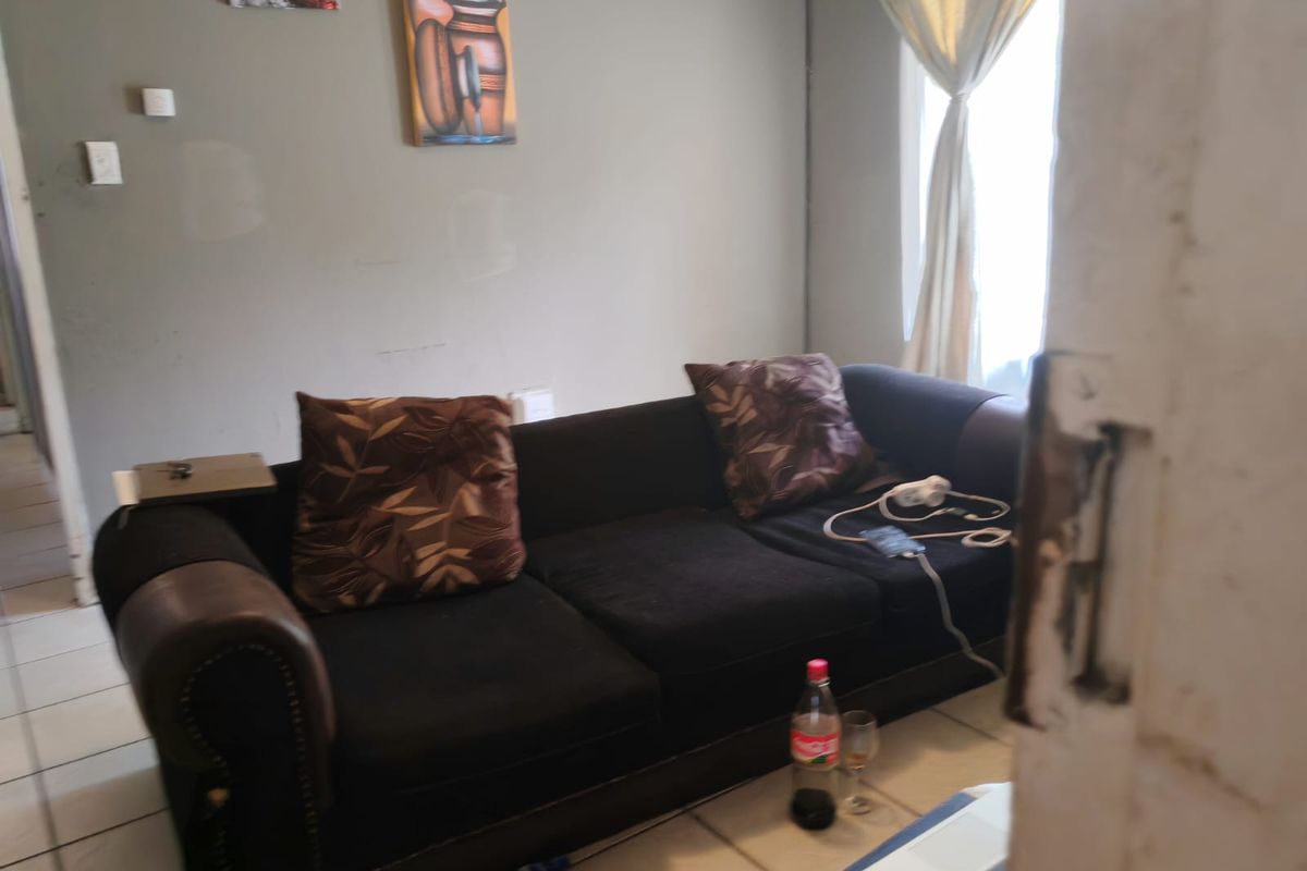 A living room area featuring tiled flooring and a window with curtains, viewed from an adjacent doorway.