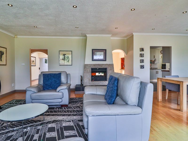 Spacious open-plan living area featuring hardwood flooring, recessed downlights, and a central fireplace with decorative stone cladding, leading into an adjacent kitchen space.