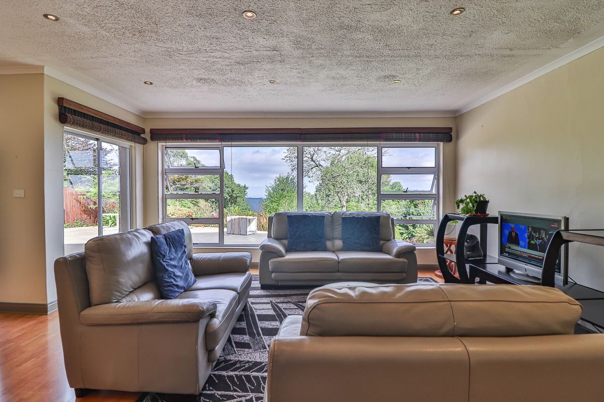 Spacious living room featuring large windows with garden views, recessed downlights, and laminate flooring, offering a bright and comfortable atmosphere.
