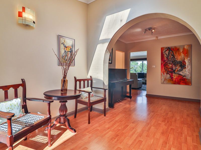 A welcoming hallway featuring warm laminate flooring, a decorative archway leading to the living area, and elegant wall lighting.