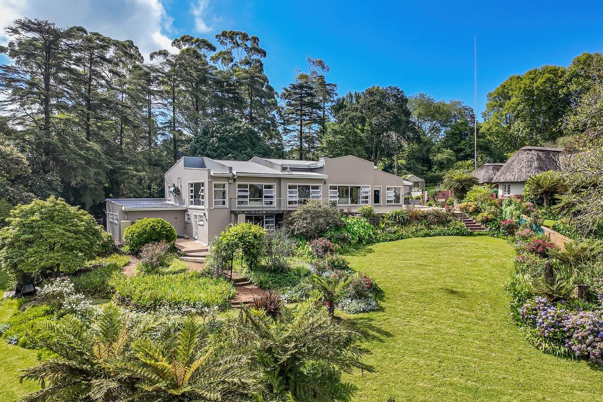 A spacious rear garden featuring a well-maintained lawn, lush landscaping, stone pathways, and timber decking leading to the main residence.