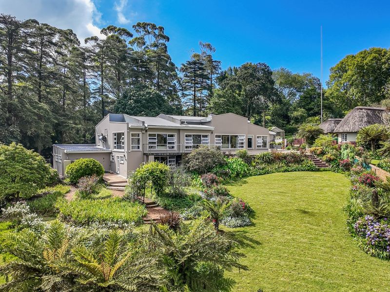 A spacious rear garden featuring a well-maintained lawn, lush landscaping, stone pathways, and timber decking leading to the main residence.