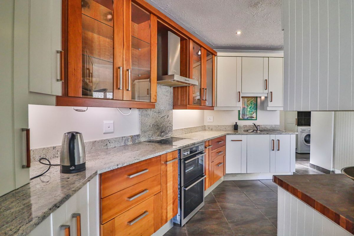 A well-maintained kitchen featuring a mix of wood and white cabinetry, granite countertops, built-in oven, and a stainless steel extractor fan.