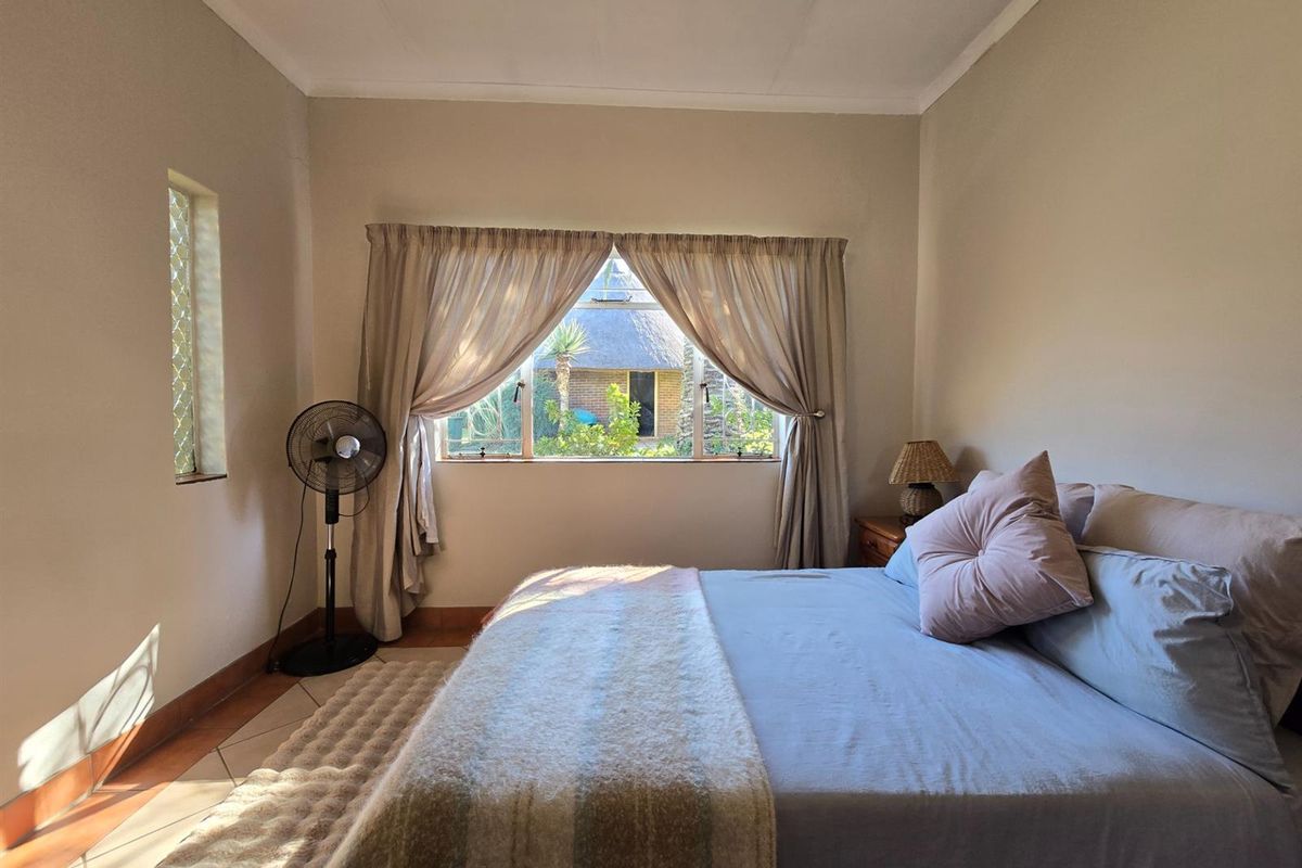 A bedroom featuring tiled flooring, neutral walls, and natural light through a window with security bars, overlooking the garden area.