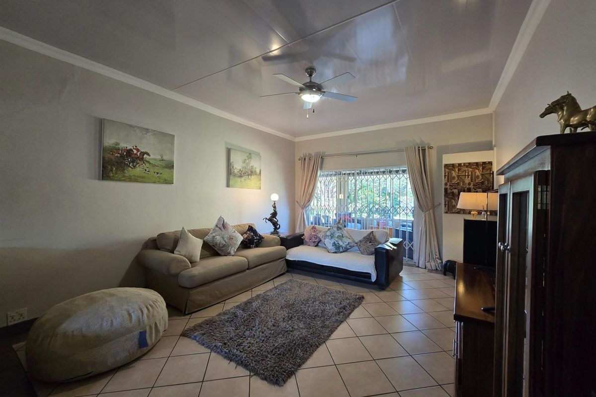 A comfortable living room featuring tiled flooring, a ceiling fan, and a sliding glass door with a security gate leading to the outdoors.