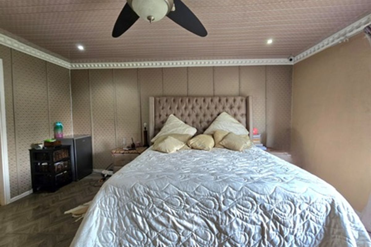 A bedroom featuring paneled walls, decorative crown molding, and a ceiling fan with integrated lighting.