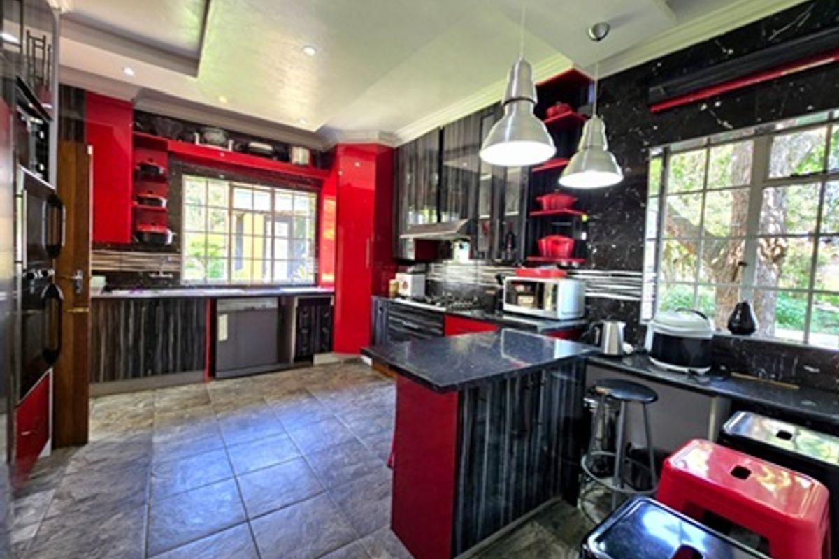 A modern kitchen featuring high-gloss red and dark wood cabinetry, granite countertops, a central island, and tiled flooring with ample natural light.