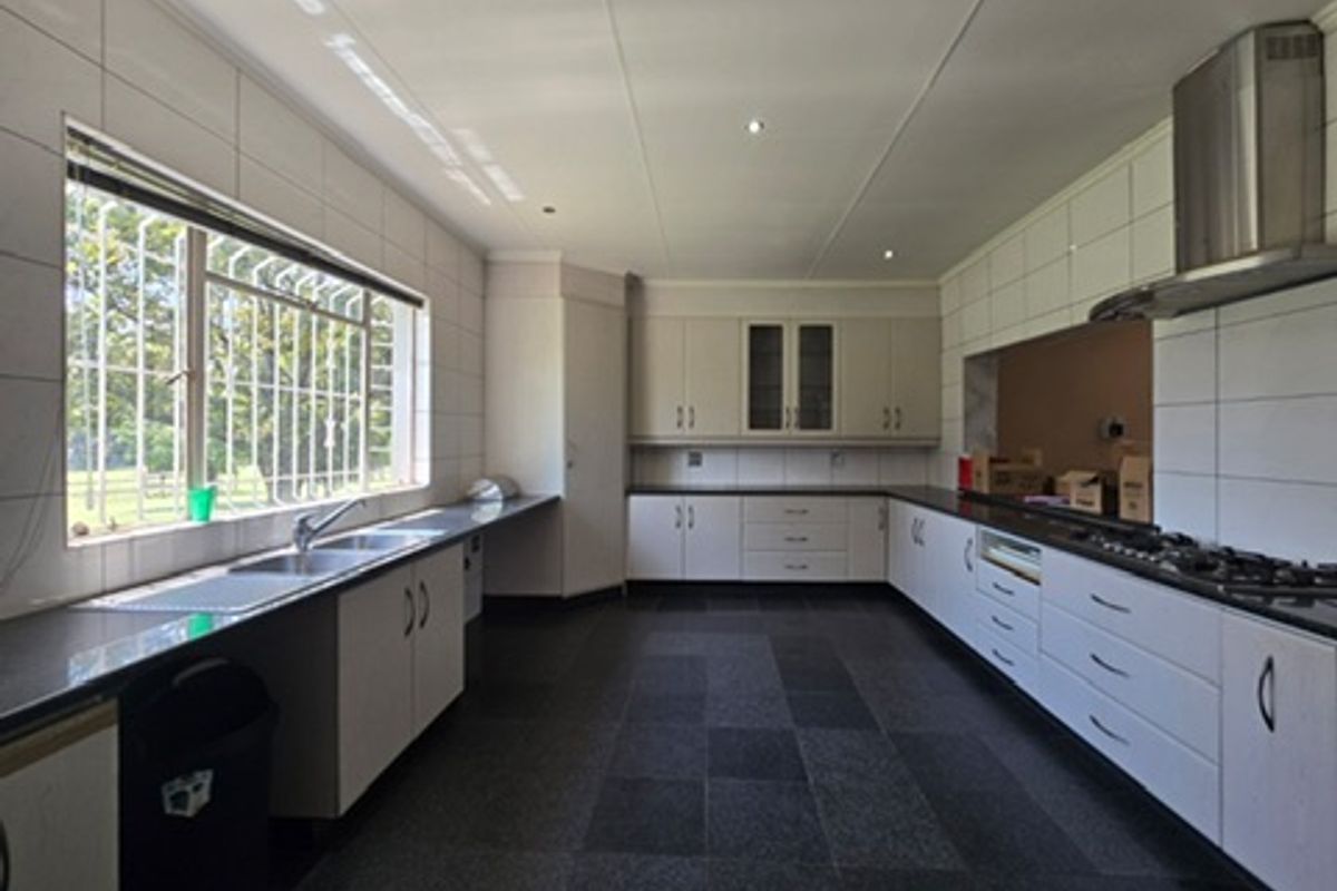 Spacious kitchen featuring extensive built-in cabinetry, a gas hob with extractor fan, double sink, and large windows with security bars.