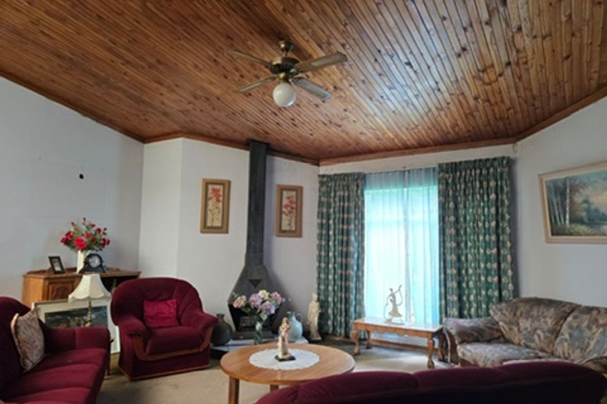 A living room featuring a distinctive wood-paneled ceiling, a central ceiling fan, and a freestanding fireplace, offering a cozy and traditional atmosphere.