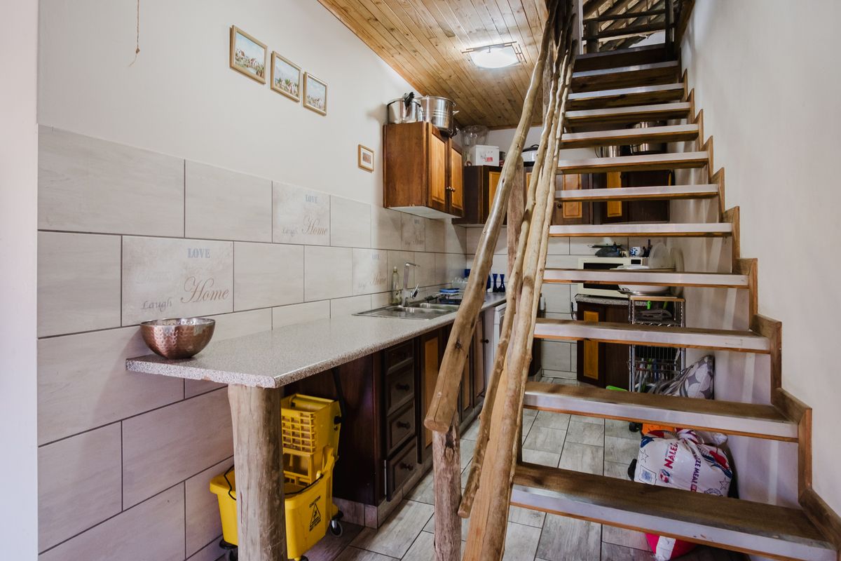 Compact kitchen area featuring built-in cabinetry, tiled backsplash, and a rustic wooden staircase leading to an upper level.
