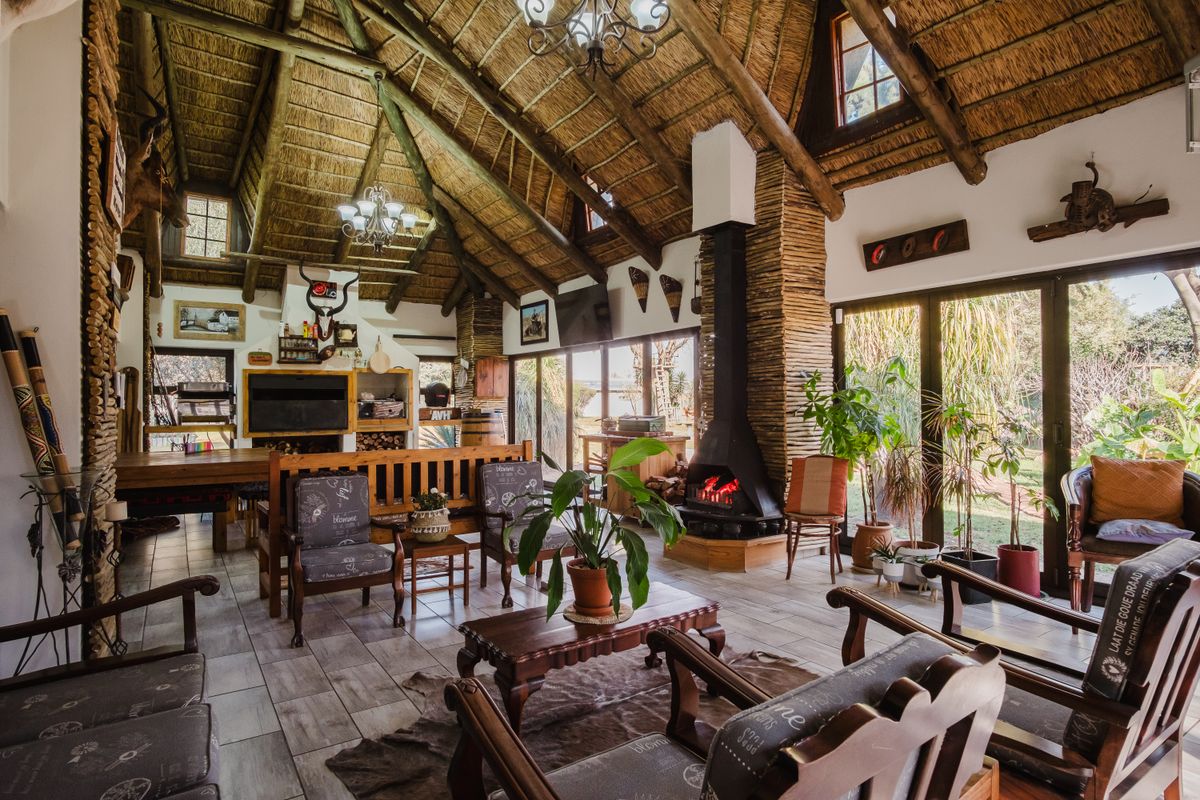 Spacious living area featuring a high vaulted thatched ceiling with exposed timber trusses, a striking stone-clad fireplace, and large glass doors opening to the garden.