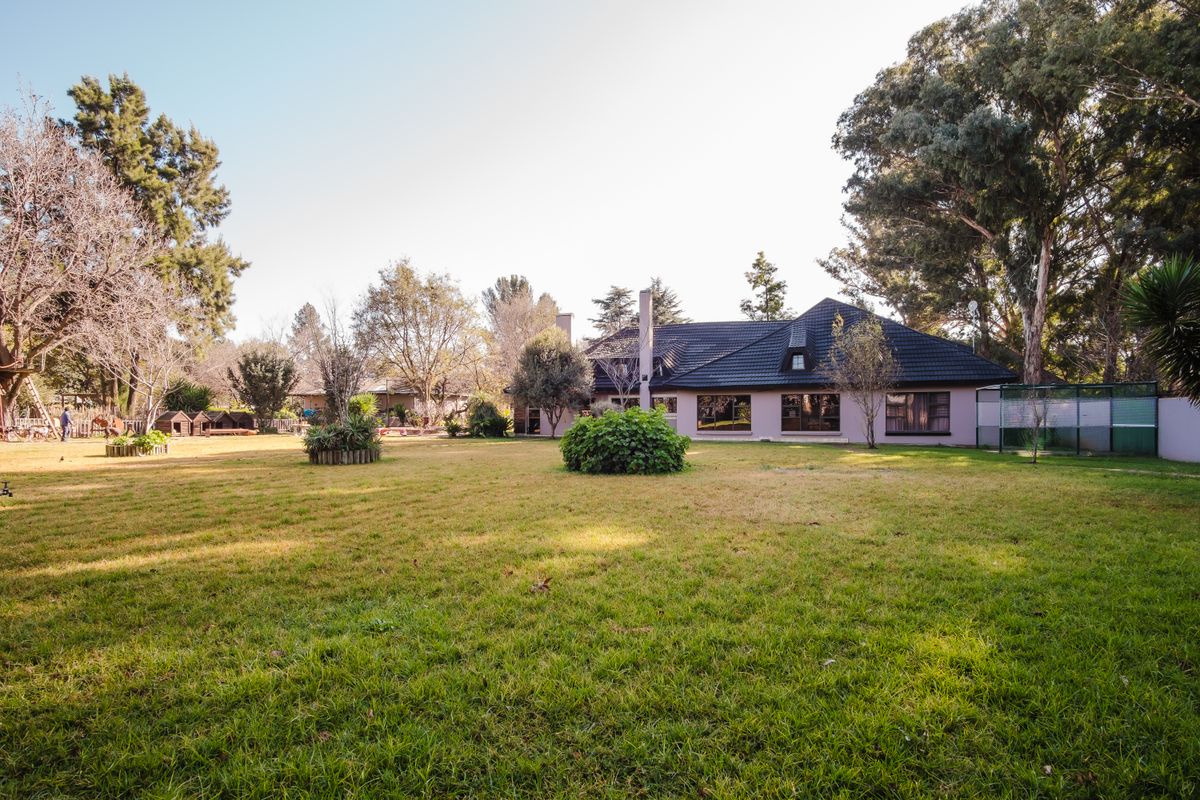 Spacious rear garden view featuring a well-maintained lawn, mature trees, and the rear elevation of the main dwelling with a tiled roof.