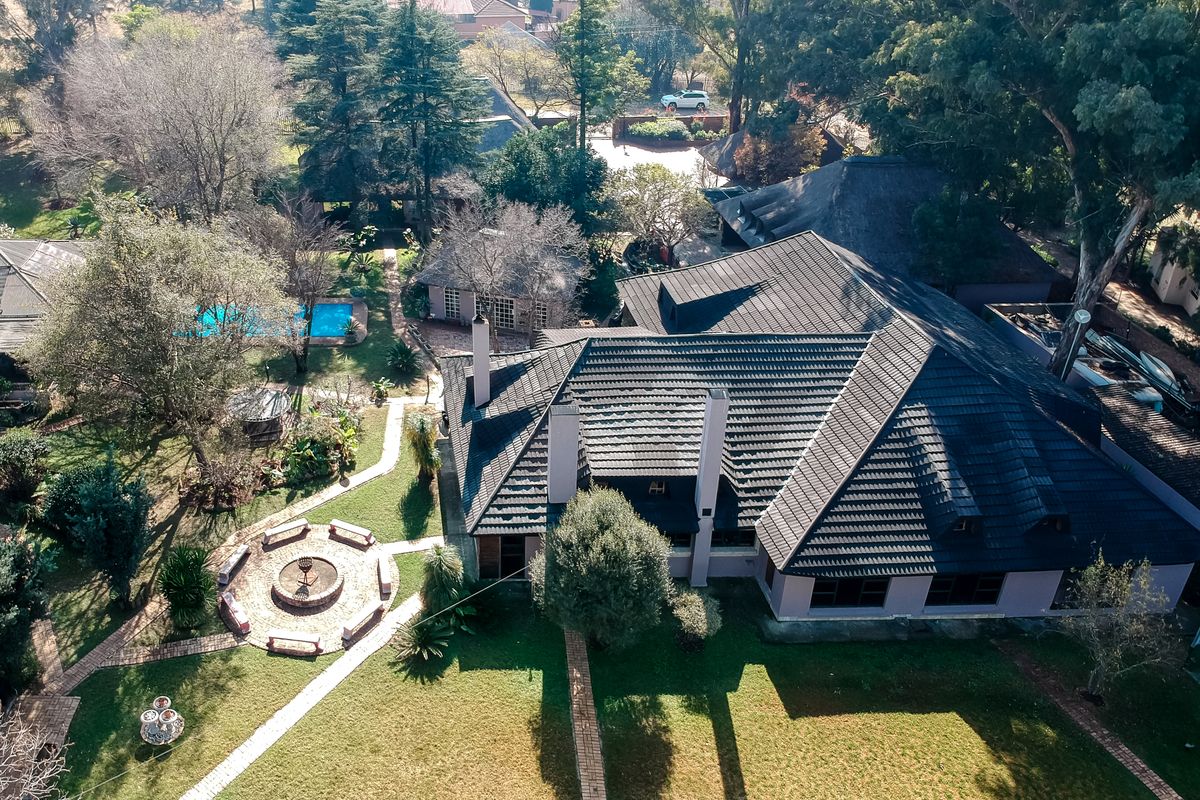 Aerial view of the property showcasing the main dwelling with a tiled roof, expansive garden, swimming pool, and a central stone fountain feature.
