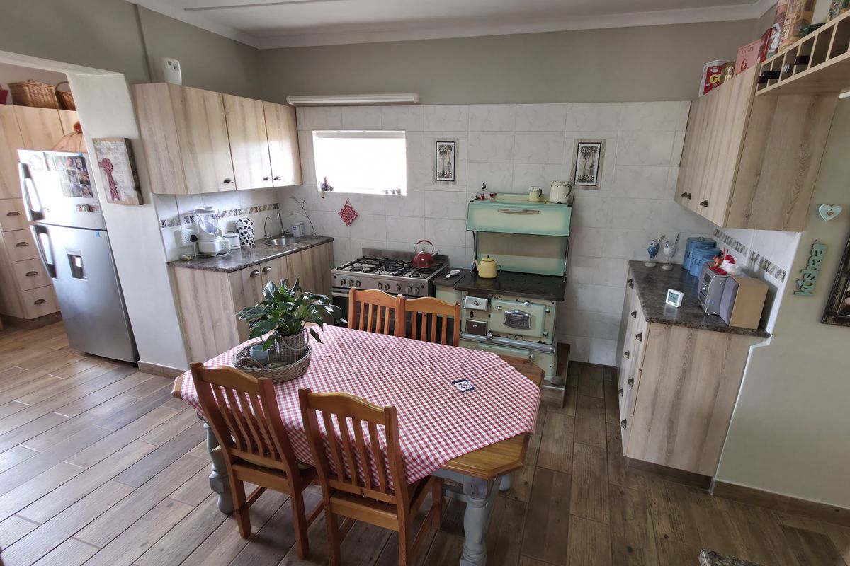 A functional kitchen featuring wood-look cabinetry, tiled splashbacks, a gas stove, and a vintage-style range cooker, with wood-effect flooring throughout.