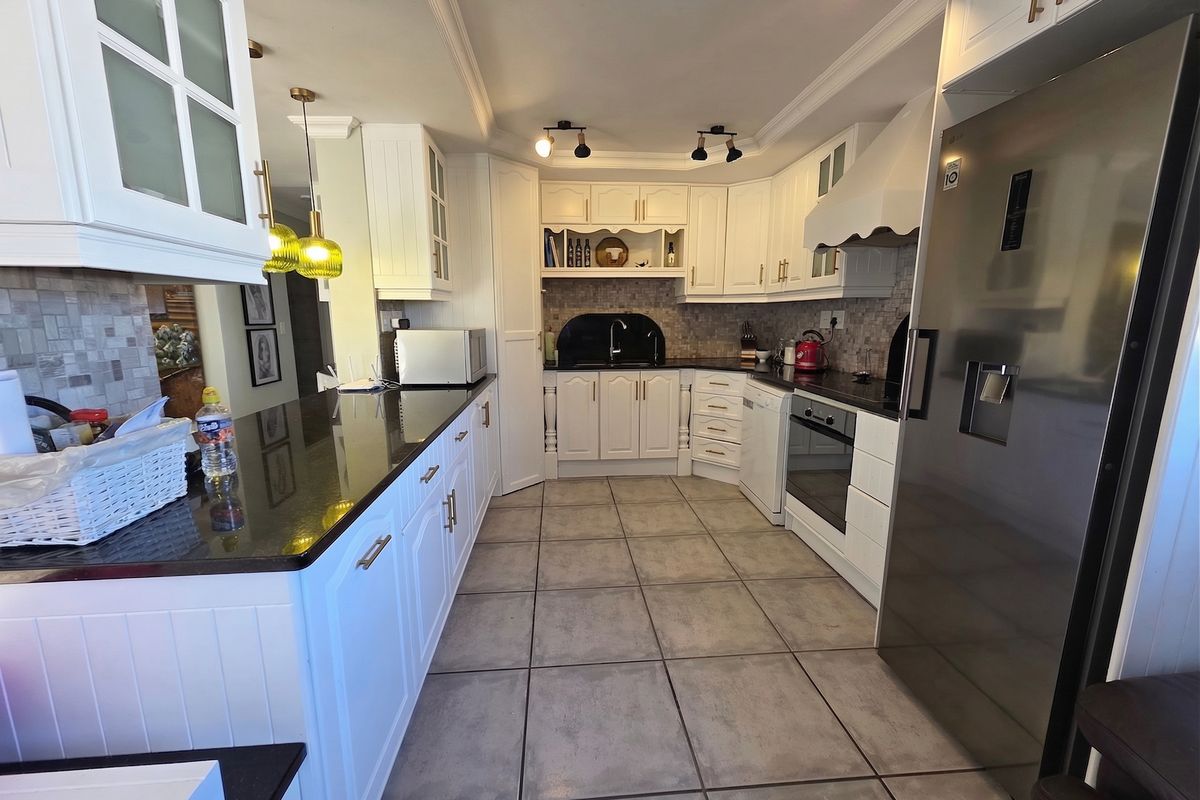 A well-maintained kitchen featuring white shaker-style cabinetry, dark granite countertops, tiled flooring, and integrated appliances, offering a clean and functional cooking space.