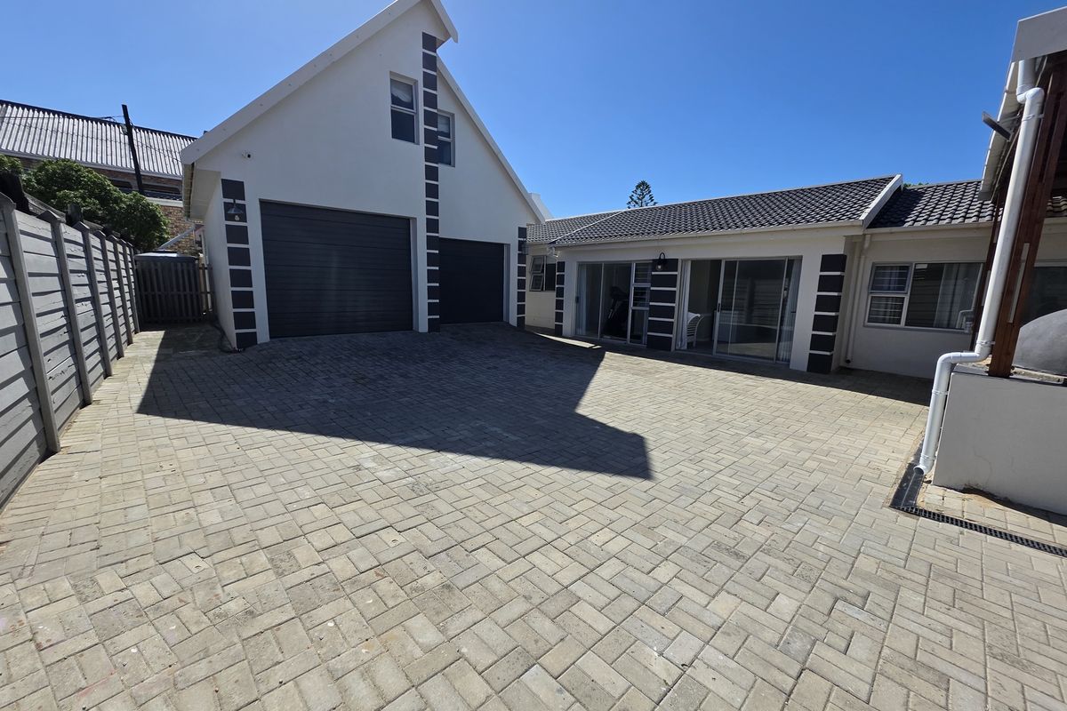 A spacious paved rear courtyard featuring a double garage and direct access to the home through sliding glass doors.