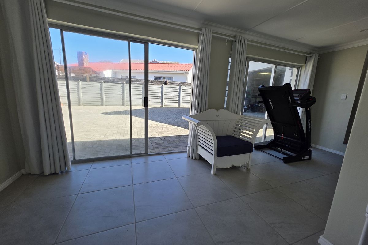 Bright living area featuring large sliding glass doors that open onto a paved outdoor space, complemented by neutral tiled flooring and recessed lighting.