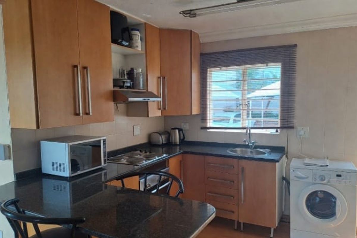 A functional kitchen featuring laminate cabinetry, granite countertops, an electric hob with extractor, and a breakfast bar for casual dining.