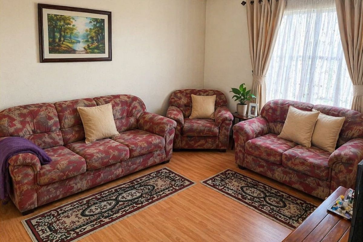 A comfortable living room featuring laminate flooring, coving, and natural light from a window with curtain fixtures.