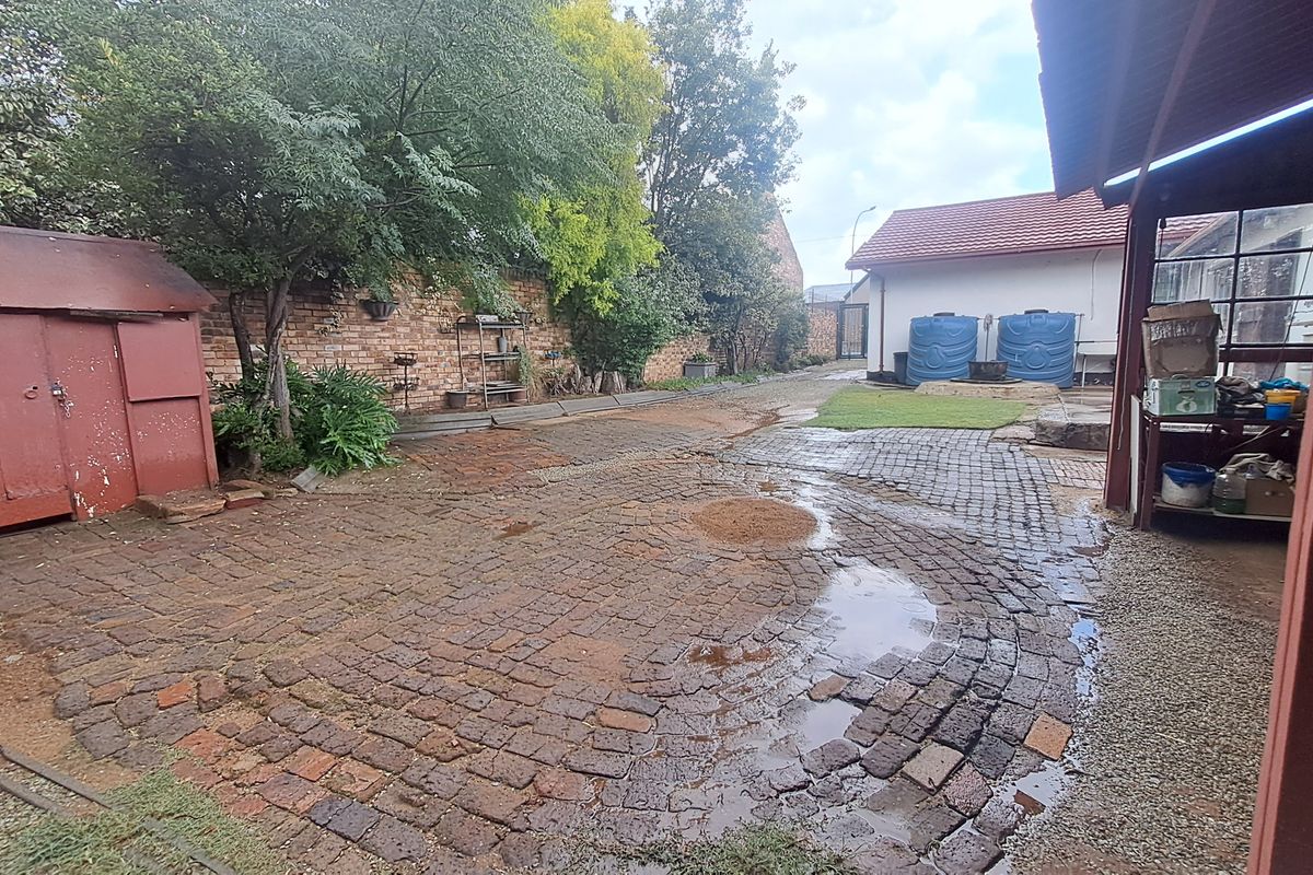 Rear courtyard area featuring brick paving, a covered patio structure, and a metal garden shed, with established boundary walls and water storage tanks.