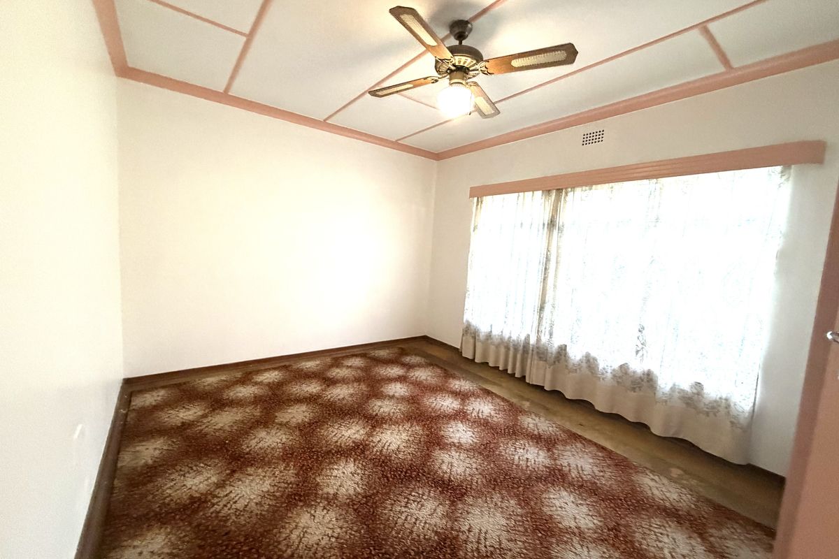 A spacious bedroom featuring patterned carpeting, a ceiling fan, and large windows with natural light, offering a blank canvas for renovation.
