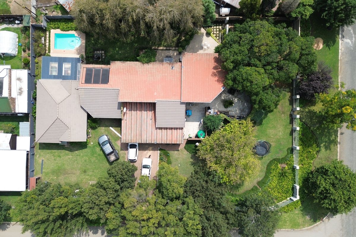 Aerial view of the property showcasing the main dwelling, swimming pool, landscaped garden, paved driveway, and surrounding mature trees.