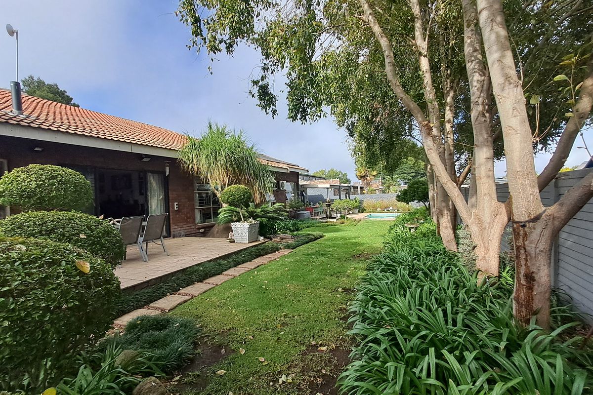 A well-maintained rear garden featuring a paved patio area, established landscaping, and a swimming pool set against the brick facade of the house.