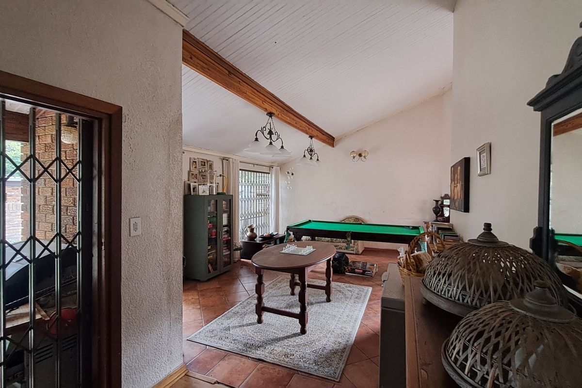 Spacious living area featuring vaulted ceilings with exposed timber beams, terracotta tiled flooring, and direct access to an outdoor patio through a security gate.