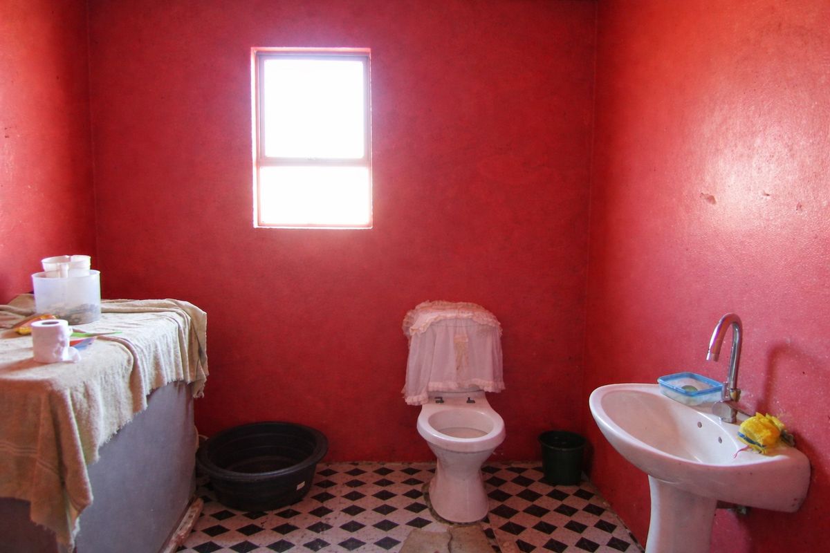 A basic bathroom featuring a pedestal basin and toilet with bold red walls and patterned floor tiles, requiring cosmetic updates.