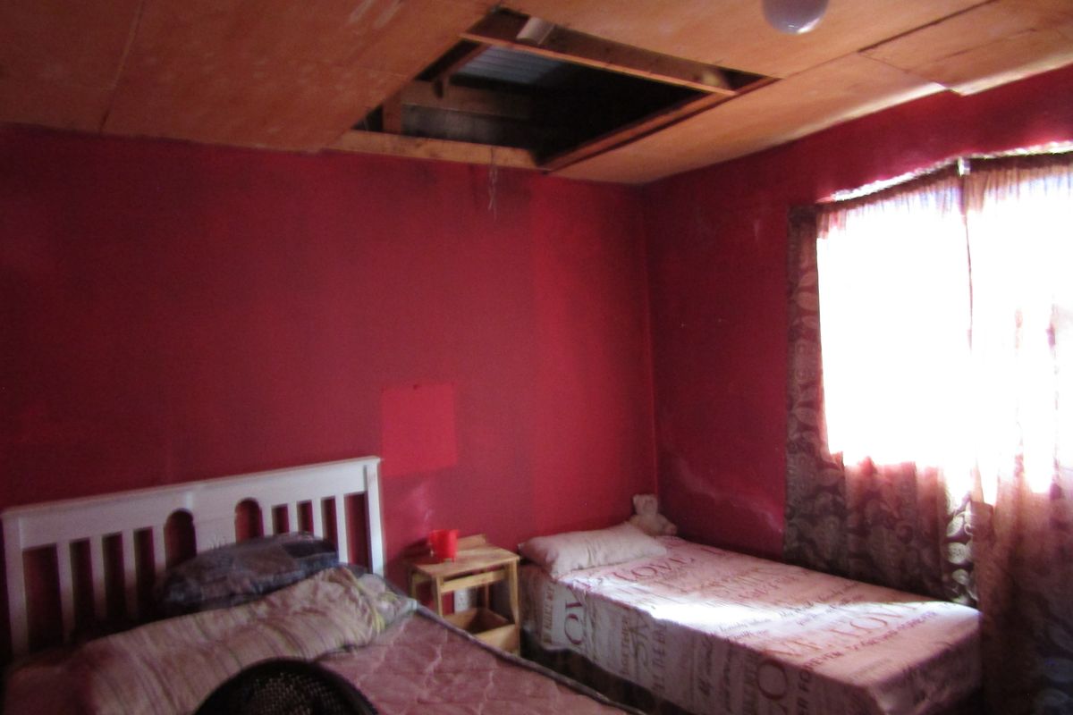 A bedroom featuring red walls and a partially missing ceiling panel, requiring significant repair and renovation to restore the space.