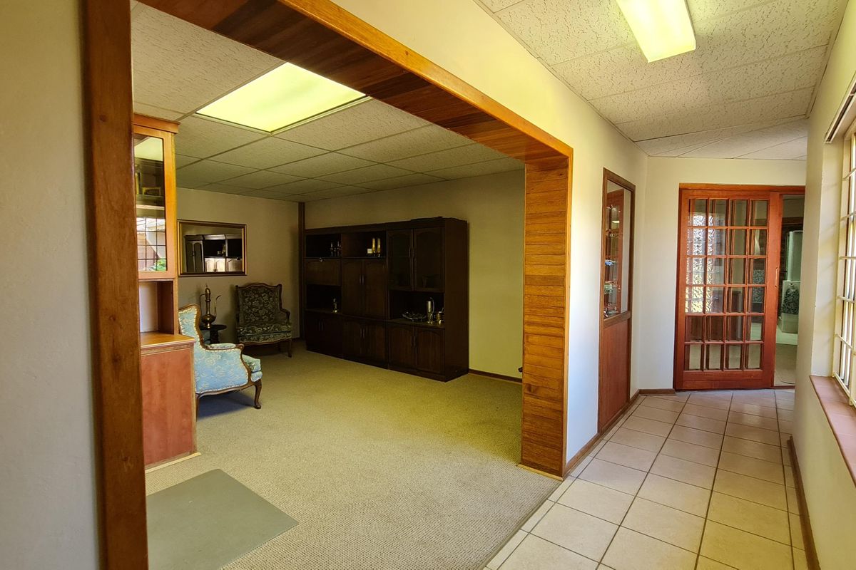 A spacious living area featuring a wooden room divider, tiled hallway, and large windows, offering a traditional layout with potential for modernization.