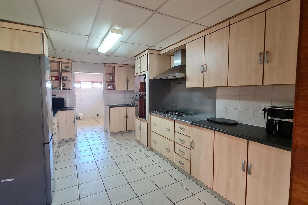 A functional kitchen featuring light wood-finish cabinetry, a stainless steel extractor fan, a gas hob, and tiled flooring with an adjacent scullery area.